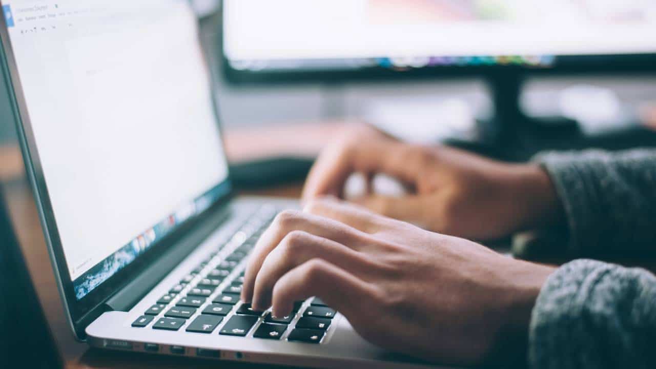 A close-up photo of a person's hands on a laptop's keyboard