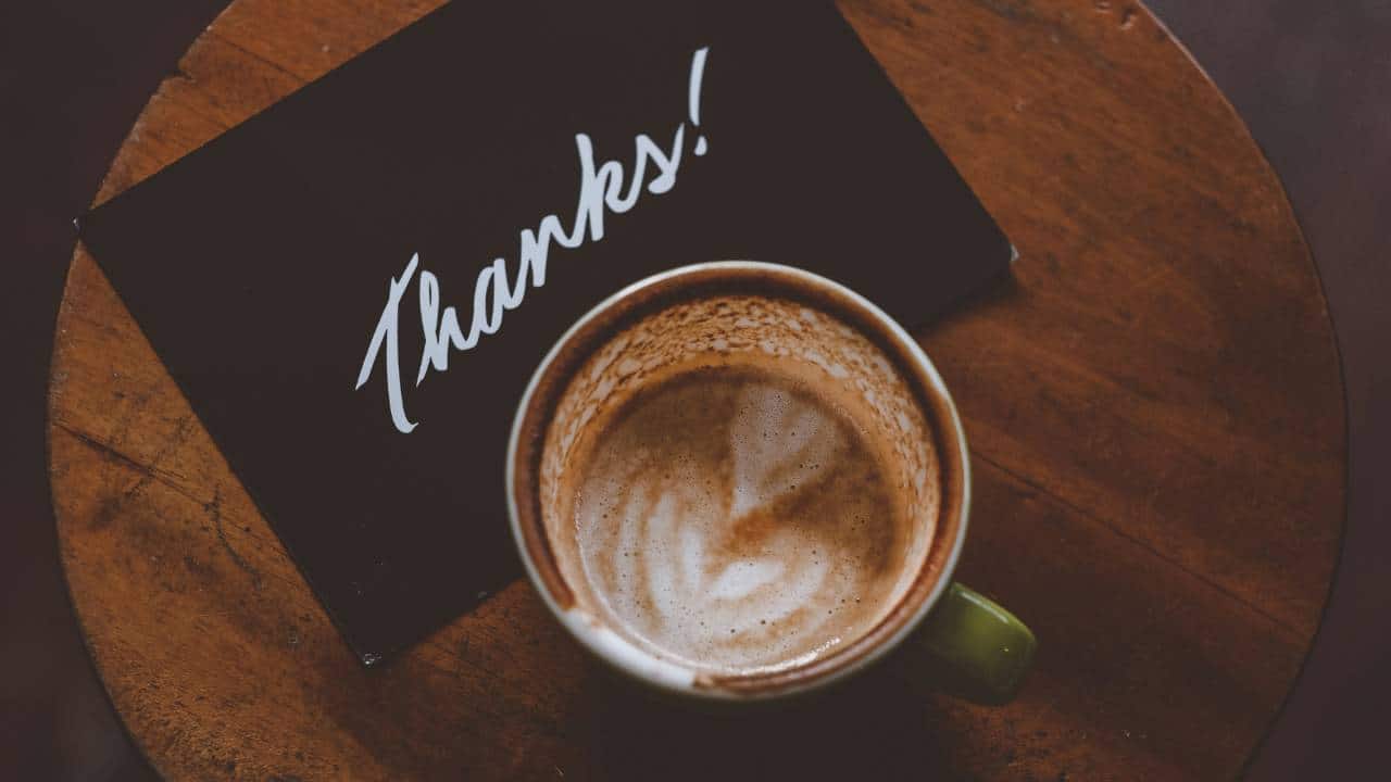 A black "thanks" card next to a cup of coffee