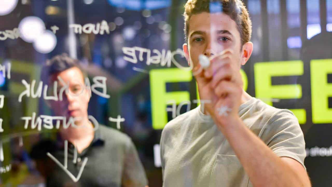 A young man using a pen to write on a transparent board