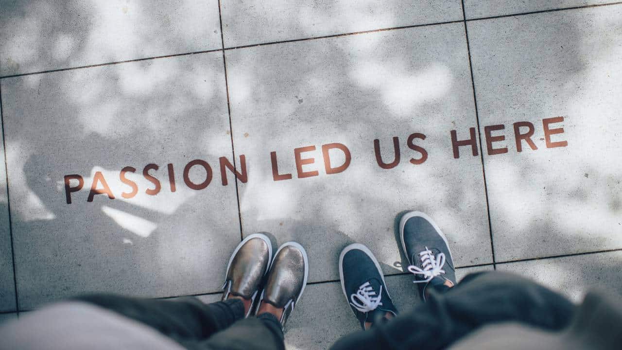 Two people standing on a sidewalk with "passion led us here" written on it