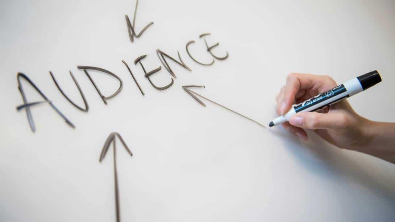 A person writing the word "audience" on a whiteboard